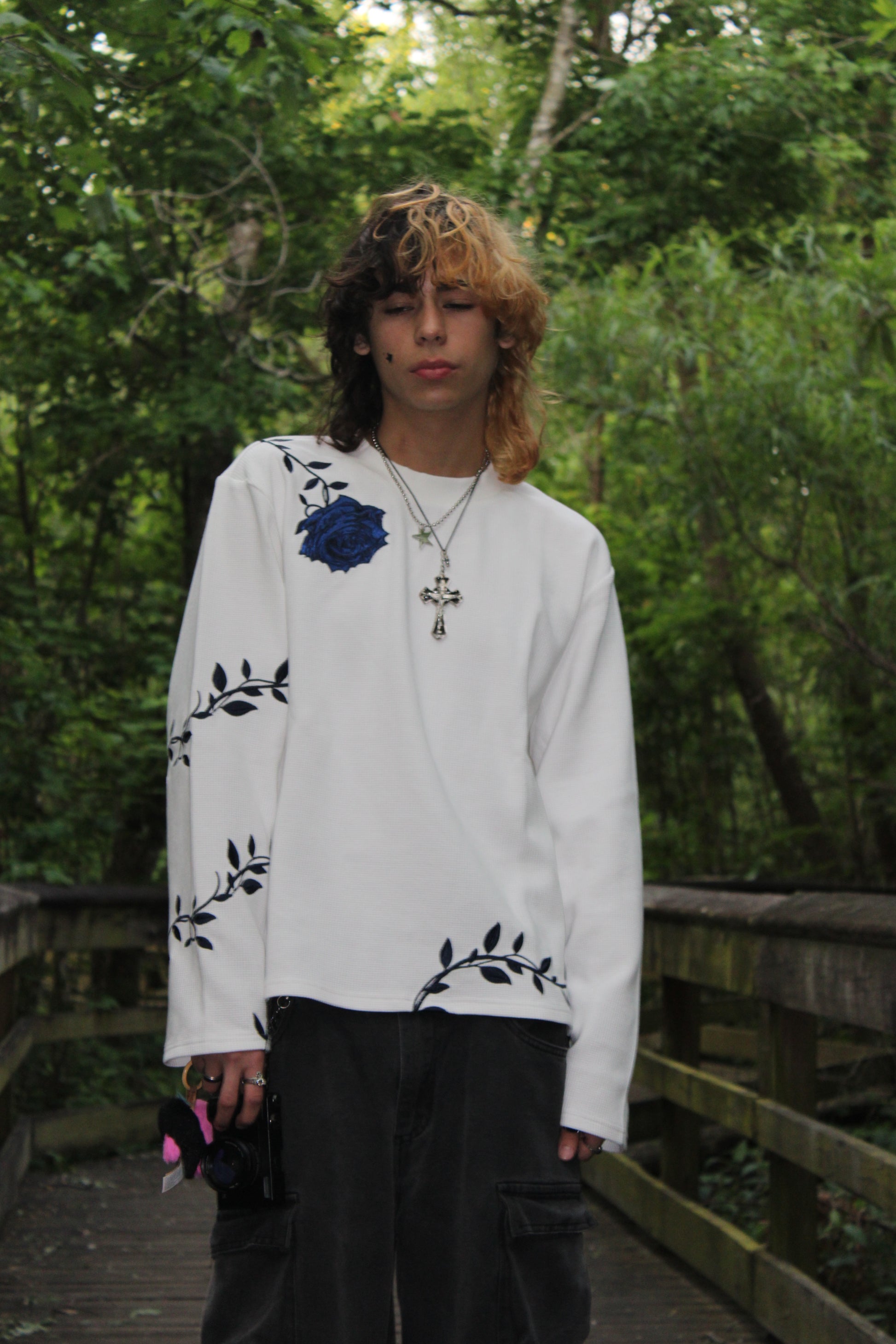 Person wearing a white outfit with black floral patterns in a forest setting