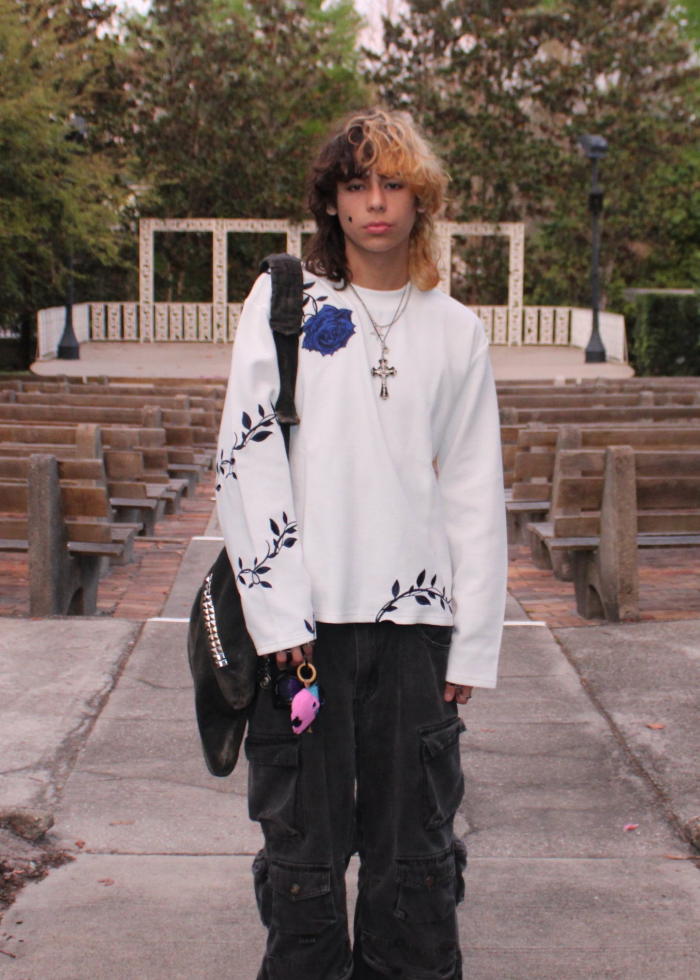 Person wearing a white sweater with black patterns and black pants, standing outdoors.
